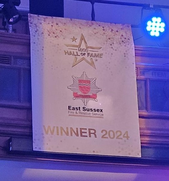 White banner with gold star IESE Hall of Fame, East Sussex FRS crest and winner 2024 in gold.