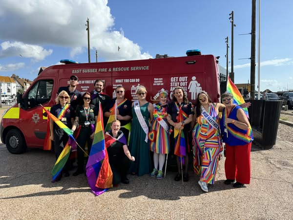 Group of people dressed in various rainbow outfits for Hastings Pride standing in front of an ESFRS van. 
